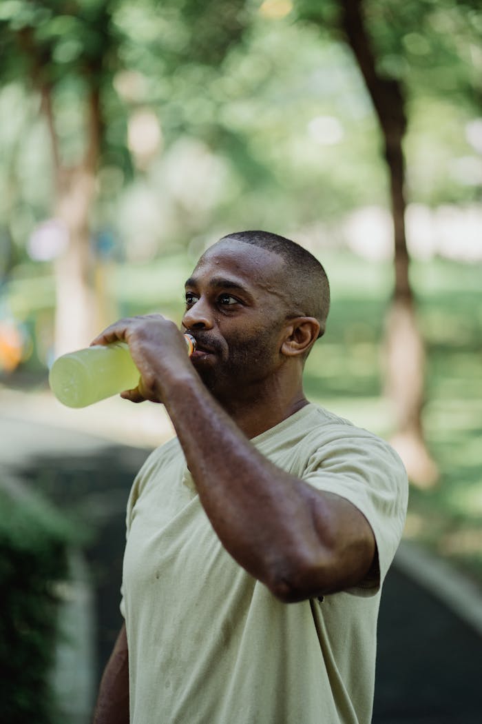 Adult man in park drinking energy drink post-workout, capturing a refreshing moment.